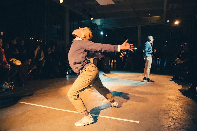 A dancer in a Donald Trump mask lunges wearing sneakers, khakis and a sweatshirt.